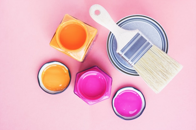 Paint cans and new brush on pink background. Focus on brush. House renovation. Color therapy