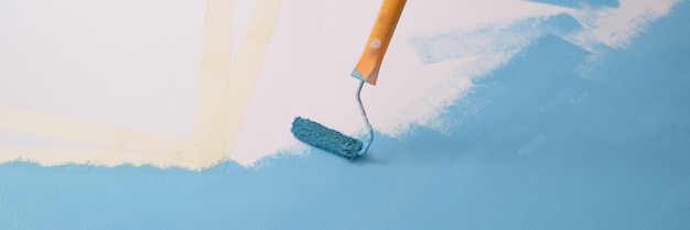 Paint roller paints white wall with blue color copy space for text art improvement and