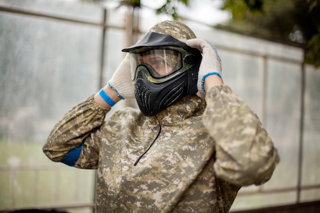 Paintball sport player in protective uniform and mask playing with gun outdoors