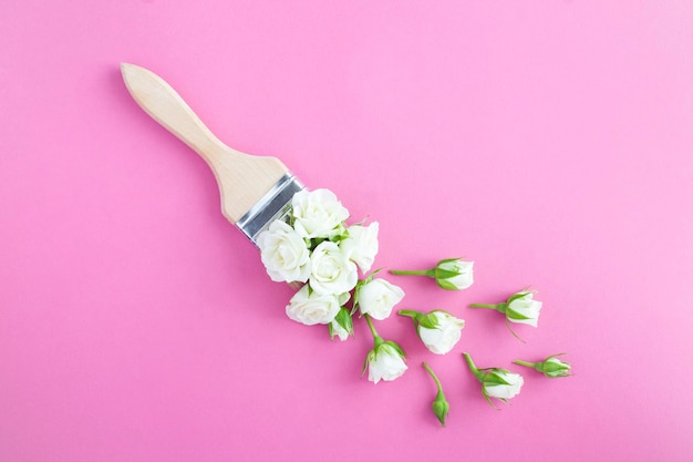 Paintbrush with white roses on the pink background Top view Copy space