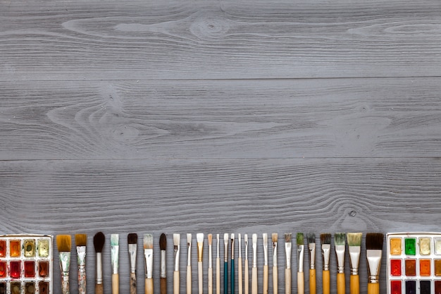 Paintbrushes set and watercolor paints on grey wooden table