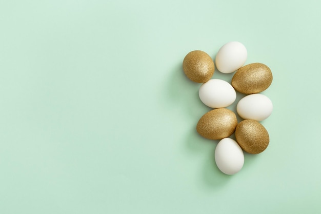 Painted Easter eggs white and gold colored on light green paper Minimal easter concept