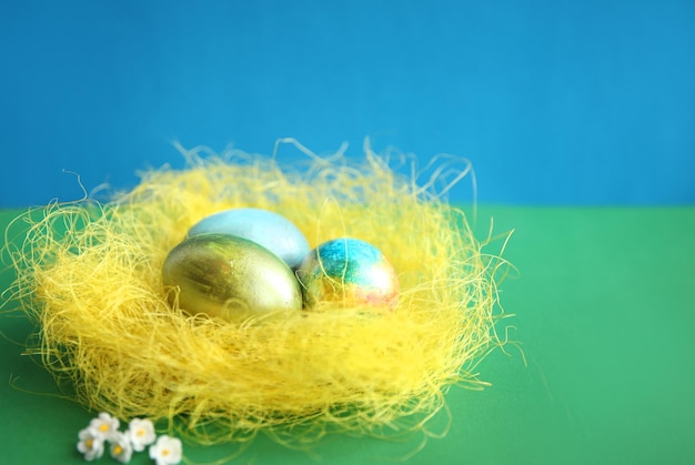 Painted Easter eggs in a yellow nest on a blue-green background, holiday concept