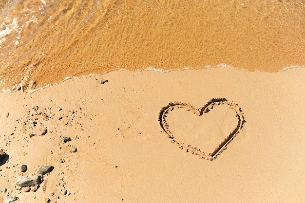 Photo painted heart on clean sand of beach and a wave of clear transparent water rolls not glossy image