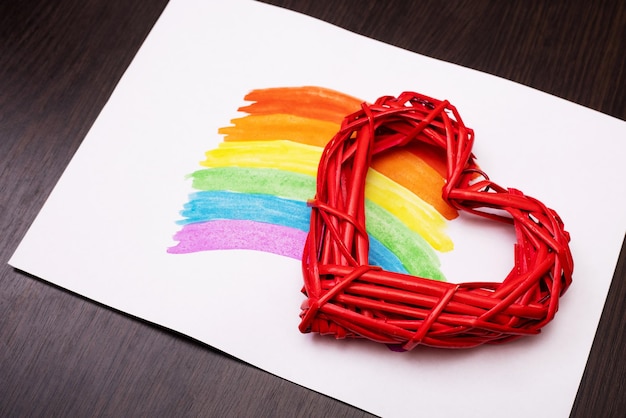 Painted rainbow on a white sheet of paper with red heart on wooden background