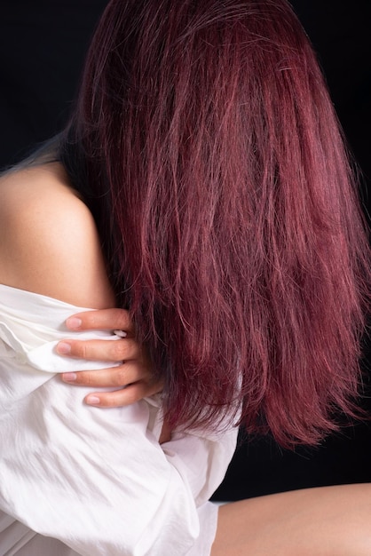 Painted redhaired girl in a boy shirt on a black background Beauty hair dyeing