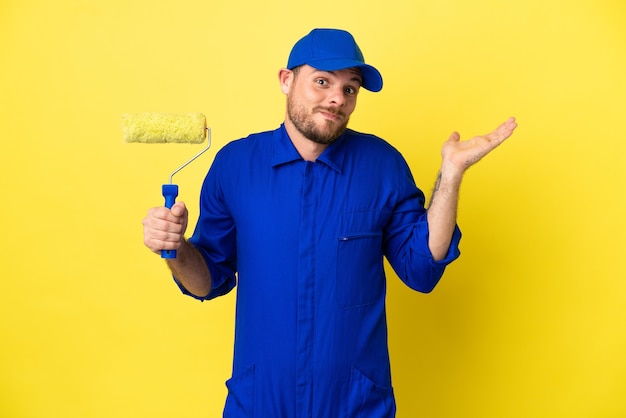 Painter Brazilian man isolated on yellow background having doubts while raising hands