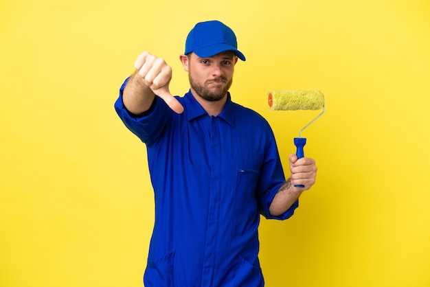 Painter Brazilian man isolated on yellow background showing thumb down with negative expression