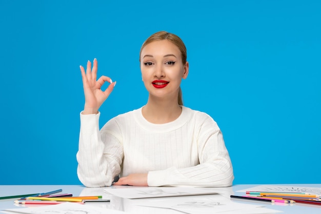 Painter cute young blonde painter girl showing ok sign and with many pencils on the table