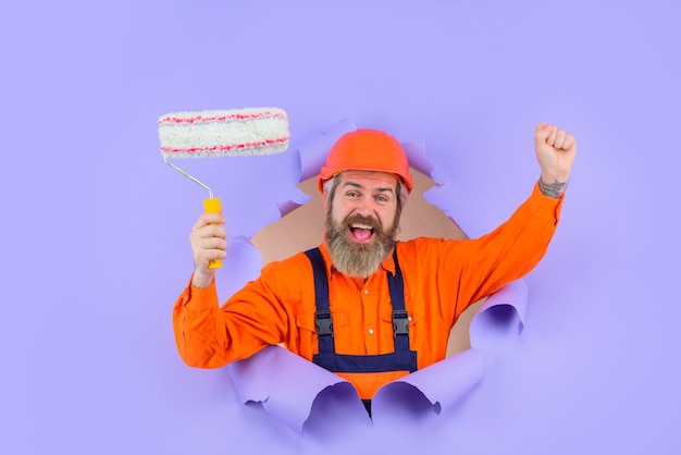 Painter painter with painting roller through hole in paper happy bearded worker with paint roller