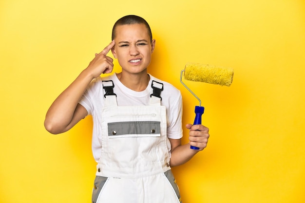 Painter woman shaved head with yellow roller showing a disappointment gesture with forefinger