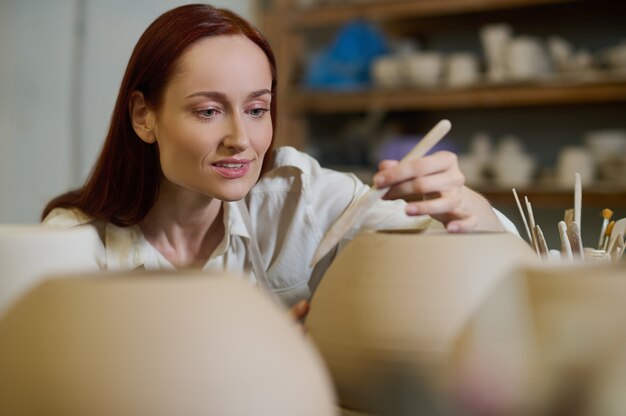 Photo painting. a cute female potter looking involved while painting the pot