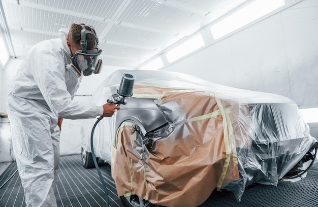 Painting job in progress Caucasian automobile repairman in uniform works in garage