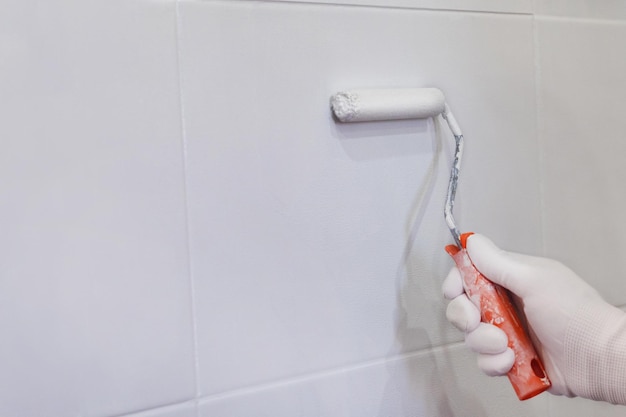 Painting tiles in the kitchen in the bathroom white paint with a roller Hand in glove with roller