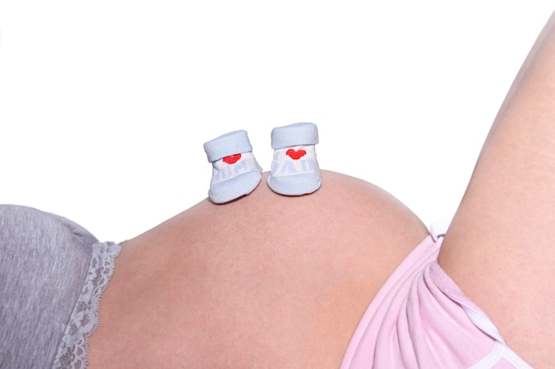 A pair of baby shoes are on the belly of a pregnant woman.