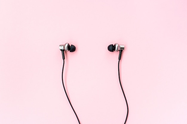 Pair of black music earphones for smartphone on a pink pastel background.