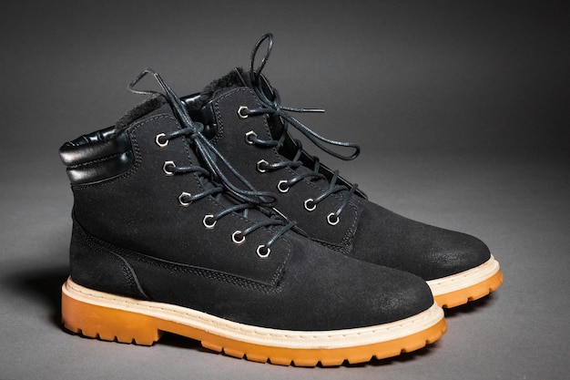 A pair of black winter men's boots with laces and a light sole on a gray background side view