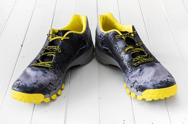 Pair of black and yellow male sport sneakers on white wooden background