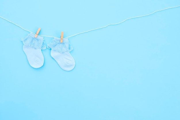 Pair blue cute baby socks hanging on the clothesline on blue background. Baby accessories. Flat lay.