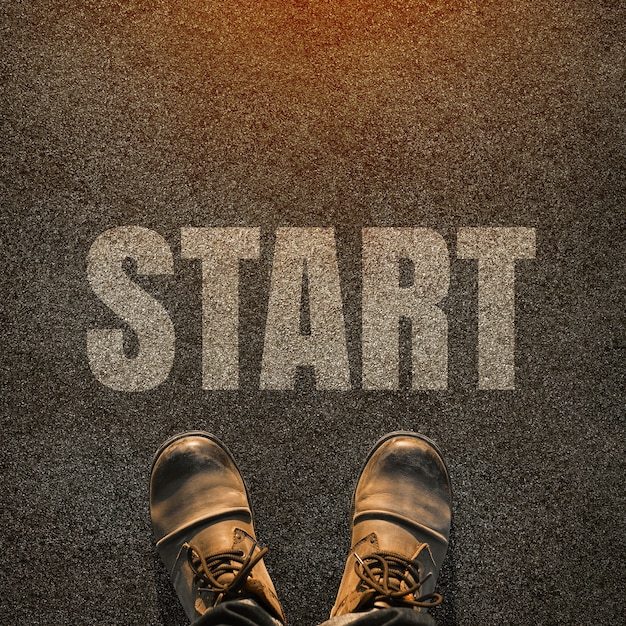 A pair of feet on a tarmac road with white print of the word start for the concept of starting point.