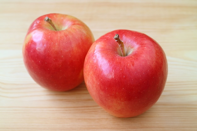 Pair of fresh vibrant red apples on light brown wooden table