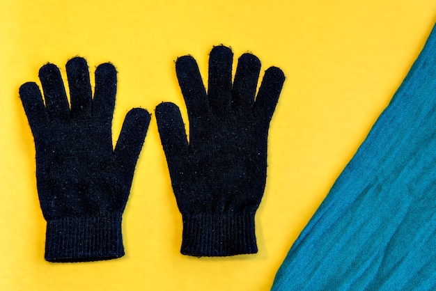 Photo pair of gloves and scarf on yellow background. top view.