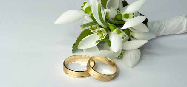 A pair of gold rings sit next to a bunch of white flowers.