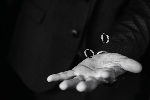 Pair of gold wedding engagement rings fly over the groom's hand in a suit