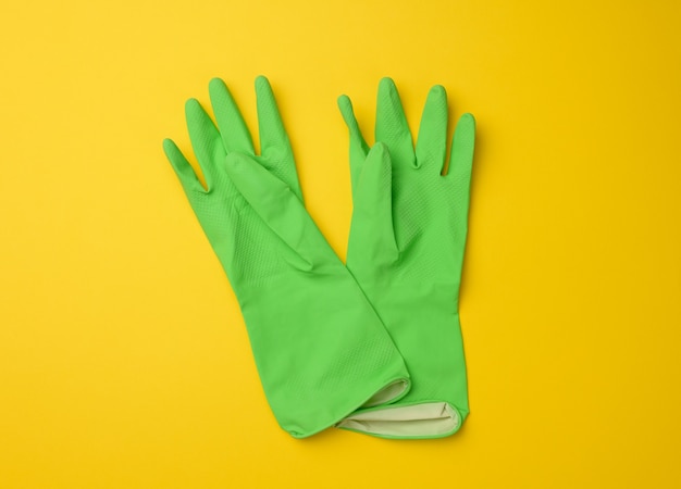 Pair of green protective rubber gloves for cleaning on a yellow background, top view