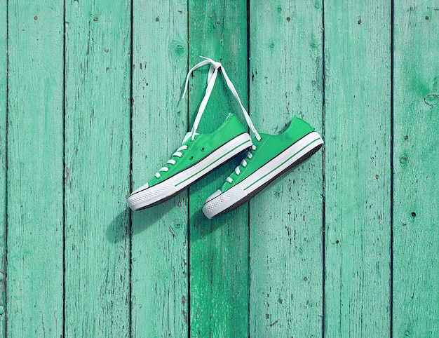 Pair of green textile sneakers hanging on a nail on the wall 