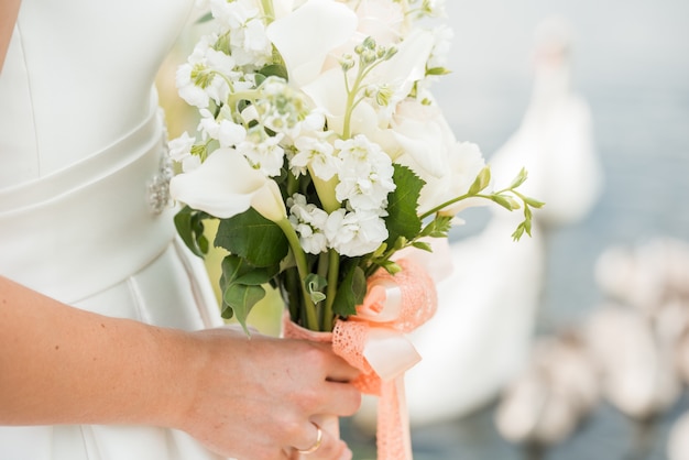 A pair of newlyweds with a bouquet of white roses sits near the lake. swan swims