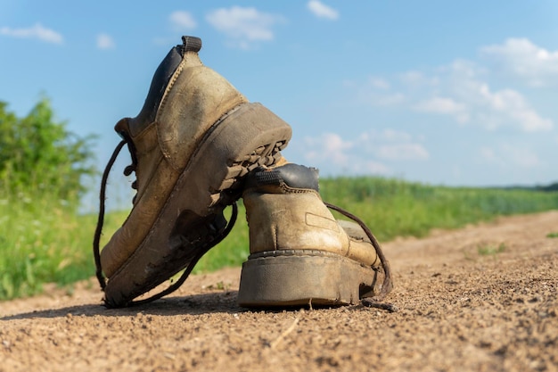 Pair of old worn leather hiking boots an a gravel path or road balanced on top of one another