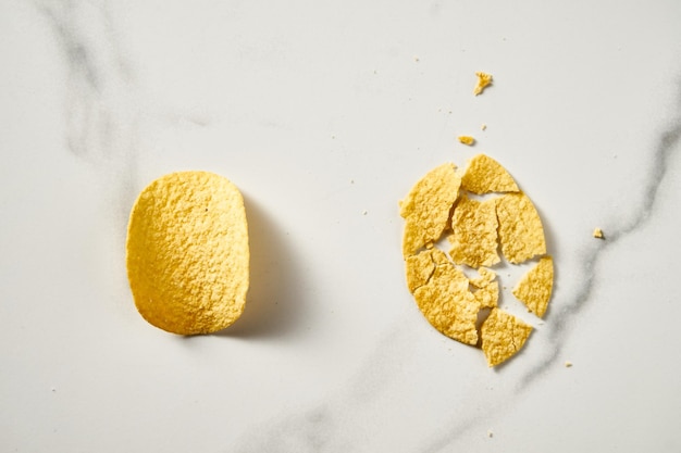 Pair of potato chips whole and broken on white marble background Minimalistic food photo