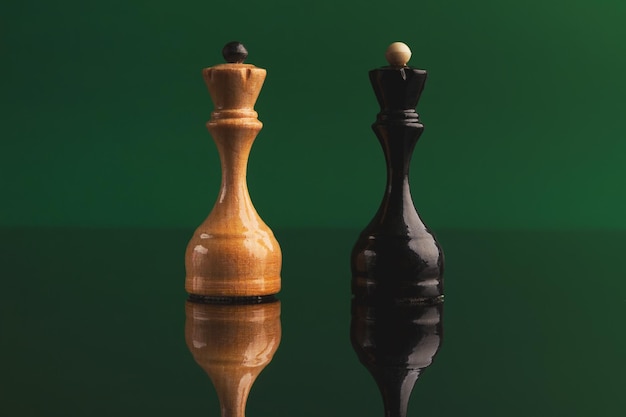 Photo pair of queen chess pieces confronted as opposites on green background with reflection. forbidden love, rival figures, copy space