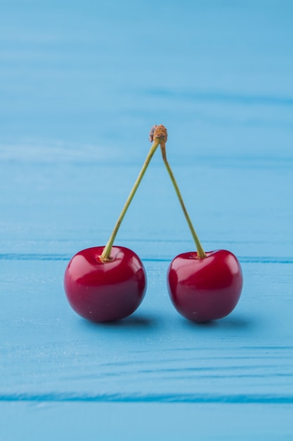 Pair of red cherries on blue wooden desk background