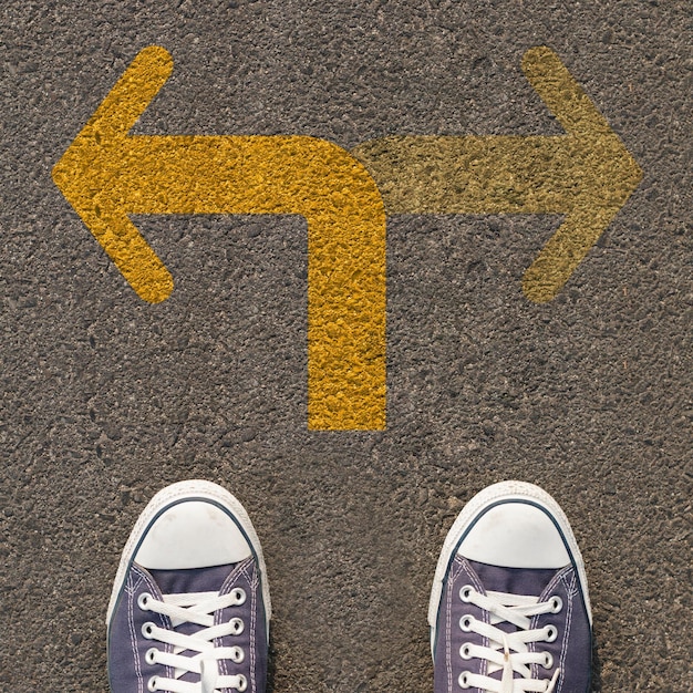 Pair of shoes standing on a road with two way yellow arrow