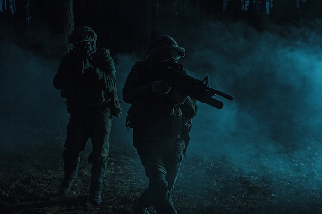 Pair of soldiers in the smoke in action on battle operation. Dark gloomy night, they moving stealthy