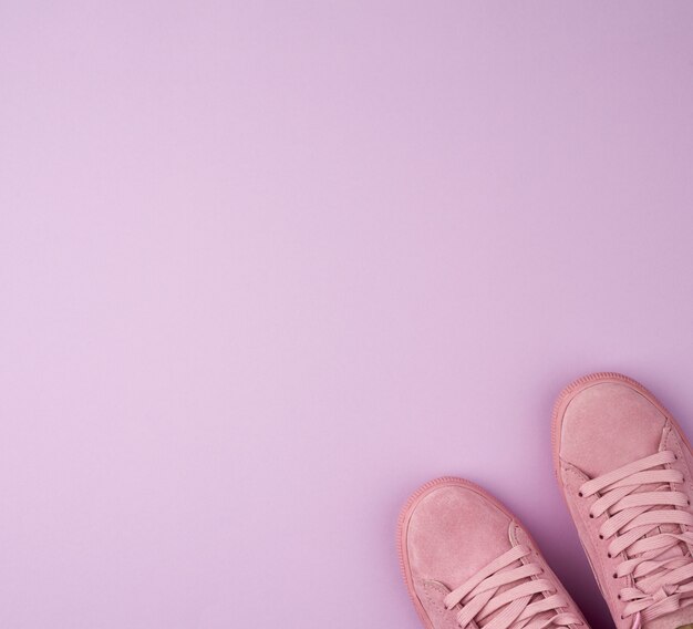 Pair of sports pink sneakers with laces on a purple background