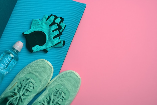 Pair of sports sneakers and a bottle with mineral water on a pink background, top view, copy space