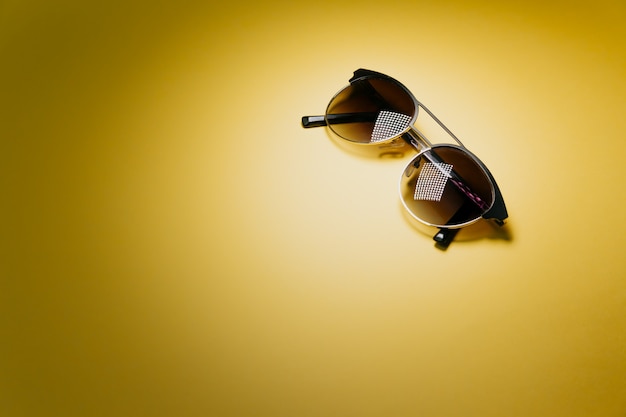 Pair of sunglasses over a pastel yellow with lights reflecting background minimal concept