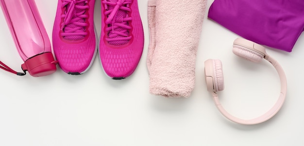 A pair of textile purple sports sneakers, wireless headphones, a towel and a bottle of water on a white background. Sportswear