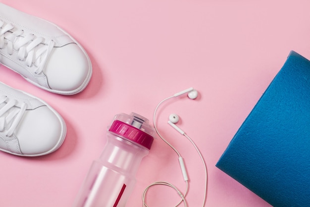 A pair of white sneakers and a sports water bottle on a pink background