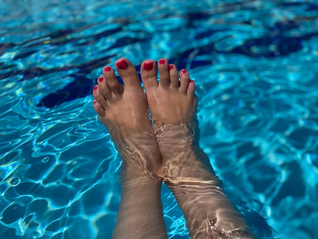 Pair of womans feet with pink manicure on blue swimming pool background