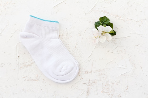 Pair of women socks and flowers of an apple tree on the white structured background, Top view.