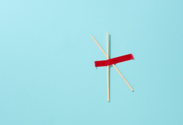 Pair of wooden sticks glued with red sticky tape on a blue background, top view