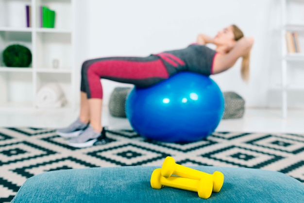 Photo pair of yellow dumbbells in front of woman exercising on blue pilates ball