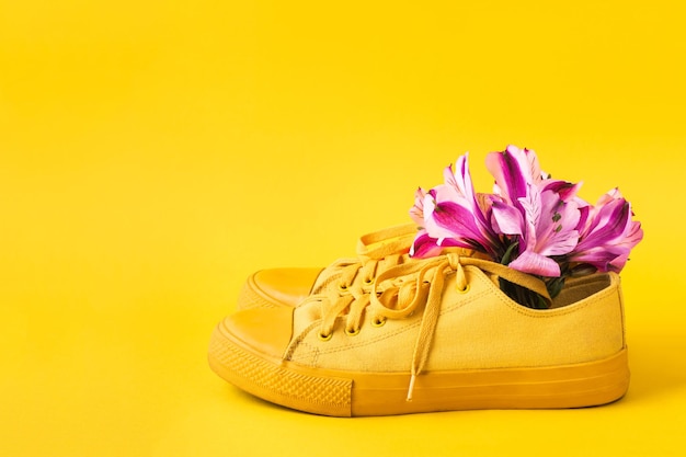 Pair of yellow sneakers and flower buds on yellow background. Spring summer fashion concept, front view, copy space.