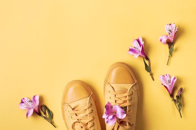 Pair of yellow sneakers and flower buds on a yellow background. Spring summer fashion concept.