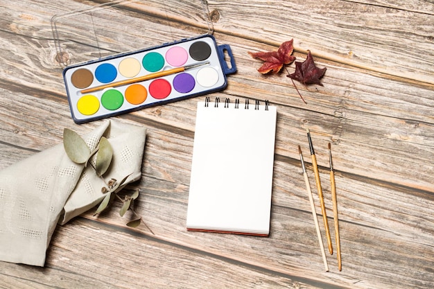 A palette of watercolors and painthbrushes on a wooden table in a top view