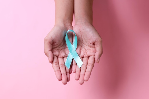 Palm hand showing teal awareness ribbon on globe over pink background